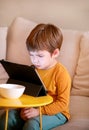 Child using tablet pc on bed at home. Cute boy on sofa is watching cartoon, playing games and learning from laptop. Education, fun Royalty Free Stock Photo