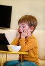 Child using tablet pc on bed at home. Cute boy on sofa is watching cartoon, playing games and learning from laptop. Education, fun Royalty Free Stock Photo