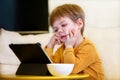 Child using tablet pc on bed at home. Cute boy on sofa is watching cartoon, playing games and learning from laptop. Education, fun Royalty Free Stock Photo