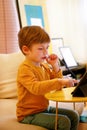 Child using tablet pc on bed at home. Cute boy on sofa is watching cartoon, playing games and learning from laptop. Education, fun Royalty Free Stock Photo