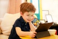 Child using tablet pc on bed at home. Cute boy on sofa is watching cartoon, playing games and learning from laptop. Education, fun Royalty Free Stock Photo