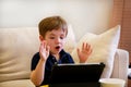 Child using tablet pc on bed at home. Cute boy on sofa is watching cartoon, playing games and learning from laptop. Education, fun