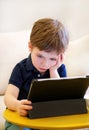 Child using tablet pc on bed at home. Cute boy on sofa is watching cartoon, playing games and learning from laptop. Education, fun Royalty Free Stock Photo