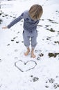 child walks barefoot on freshly fallen snow in winter. A heart is drawn on the snow