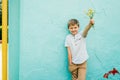 Child by the wall, baby fashion concept. cute boy outdoors in summer. Kid holds out a field bouquet of flowers