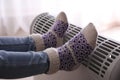 Child warming feet on electric heater at home, closeup