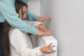 Child warming hands on heating radiator near white wall, closeup