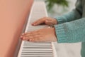 Child warming hands on heating radiator indoors, closeup