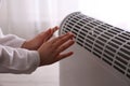 Child warming hands near electric heater at home, closeup