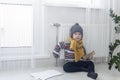 The child is warmly dressed in a sweater and a hat, sitting and holding on to the radiator. The concept of the economic crisis and