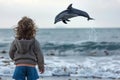 child watching a dolphin arc over sea from the shore