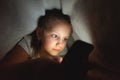 Child watching video smartphone under the blanket on the bed at night when light flashes bounce off the screen, children