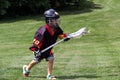 Child wearing black jersey and protective equipment playing lacrosse in the park