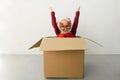 A child wearing funny Christmas glasses and Santa hat raised her hands up while sitting in a cardboard box against white Royalty Free Stock Photo