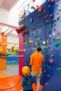 Child wearing a harness is climbing an indoor artificial wall