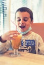 Happy child wearing a mask in a cafe during a pandemic. A boy in a cafe drinks sea buckthorn tea in a cafe during a pandemic.