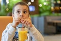 A child wearing a mask in a cafe during a pandemic. A boy in a cafe drinks sea buckthorn tea in a cafe during a pandemic