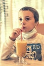 A child wearing a mask in a cafe during a pandemic. A boy in a cafe drinks sea buckthorn tea in a cafe during a pandemic. toned