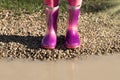 Child wearing new pink rain rubber boots standing near muddy puddle