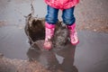 Child wearing pink rain boots jumping into a puddle