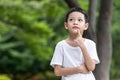 A child wearing a white t-shirt looks smart-looking up in doubt. Little Asian boy thinking with hand on chin Royalty Free Stock Photo