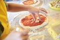 Child wearing yellow apron, putting ingredients dough on the table. Close-up picture of hands, making topping for pizza. Bakery