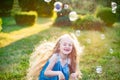 Child whirling, dancing plays on the meadow. Girl having fun with bubbles. Cute little longhair blonde girl dancing with soap