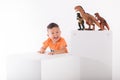 A child on a white background smiling next to a standing three dinosaur