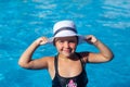 Child in white panama hat looks at camera. Happy charming tanned girl in black swimsuit stands in water and holds white Royalty Free Stock Photo