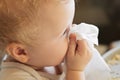 child wipes his nose with white handkerchief. sick child eats sitting on feeding chair. Kid with cold rhinitis. virus and