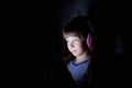 The child in wireless headphones listens to music at night under a blanket and looks at the tablet.