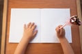 A child writes in an empty notebook on a wooden desk background. Back to school concept. Top view