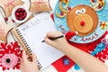 Child writes letter for santa, wish list to Christmas on table w