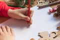 Children`s hand writes with a pencil. Child`s hands, the sheet of paper, pencils and Christmas decorations on a wooden