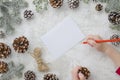 Child writes the letter to Santa Claus. Child`s hands, the sheet of paper, red pencil and Christmas decorations pine