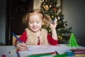 A little girl draws with crayons on the background of the Christmas tree. the concept of new year kids creativity Royalty Free Stock Photo