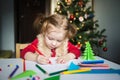 The child writes a letter to Santa Claus. a little girl draws with crayons on the background of the Christmas tree Royalty Free Stock Photo