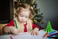 The child writes a letter to Santa Claus. a little girl draws with crayons on the background of the Christmas tree Royalty Free Stock Photo