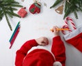 Child writes the letter to Santa Claus. Child`s hands, the sheet of paper, pencils and Christmas decorations on a wooden surface.