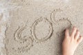 A child is writing a finger on the sand of the word SOS