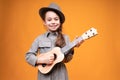 A child of 9 years old in a dress and hat smiles broadly and plays the guitar Royalty Free Stock Photo