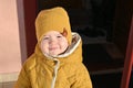 A child in yellow clothes. Dressed in a warm hat and jacket. The sun shines on a childs face