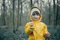 Child in yellow raincoat with hood stands in forest and holds spring flowers Royalty Free Stock Photo