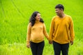 Childbearing couple hold hands and look at each other, over fresh rural country landscape