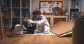 Childhood activities. Little boy in astronaut suit enters room with big cardboard piece, tool box to build space ship. Royalty Free Stock Photo