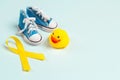 Childhood cancer awareness golden ribbon with baby shoes and rubber duck on  blue background with copy space Royalty Free Stock Photo