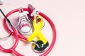 Childhood Cancer Awareness Golden Ribbon with baby sneakers and stethoscope on pink background Royalty Free Stock Photo