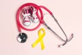 Childhood Cancer Awareness Golden Ribbon with blue baby sneakers and stethoscope on pink background with copy space Royalty Free Stock Photo