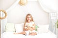 Childhood concept. Child playing in bed in a white bedroom. Children`s room and interior design. Little girl in pajamas at home. T Royalty Free Stock Photo