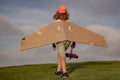 Childhood dream imagination concept. Happy kid playing with toy paper wings outdoors in summer field. Travel and kids